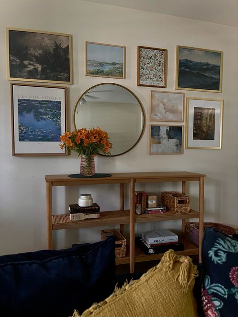 Entryway gallery wall including impressionist art prints and a gold mirror. A light wood console bookcase and lightly styled shelves with a few classic books, fashion books, and candles. Gallery Wall Console Table, Wall With Console Table, Gallery Wall Above Console Table, Mirror And Picture Wall Layout, Gallery Wall With Mirror, Entry Way Gallery Wall, Picture Wall Layout, Large Circle Mirror, Entryway Gallery Wall