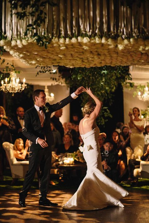 Classic white and green wedding in Santa Barbara ballroom by Beth Helmstetter Events. Impactful floral installment above wood dance floor with hanging greenery and crystal chandeliers. Bride and groom dancing on custom dance floor, beautiful first dance under hanging white roses by Beth Helmstetter. Wood Dance Floor, Custom Dance Floor, Traditional White Wedding, Wedding Santa Barbara, Bride And Groom Dancing, Hanging Greenery, White And Green Wedding, Reception Design, Crystal Chandeliers