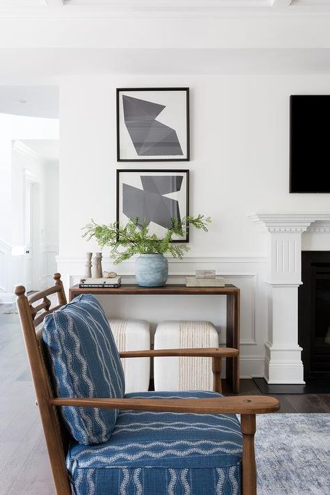 Stacked black abstract art above a wood console table styled with a floral vase and minimal accents in a living room beside a fireplace design. Table Next To Fireplace, Console Tables In Living Room, California Casual Living Room, Burled Wood Coffee Table, Casual Living Room, Console Table Styling, Vintage Style Rugs, Console Table Design, Custom Dining Tables