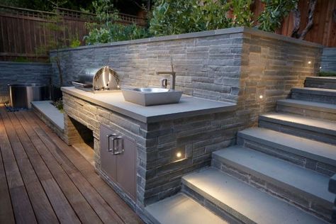 What a fantastic way to utilize and easily decorate a contemporary outdoor kitchen space! The stone retaining walls add so much charisma to the scene. The cooking ware and sink add enough interesting perspective as it is, but the effortlessly cool surrounding area makes the outdoor kitchen that much more elegant. This would be an ideal setup for entertaining or hosting a cocktail barbecue. Perfect for those long summer nights. Backyard Retaining Walls, Landscape Yard, Outdoor Kitchen Countertops, Outside Room, Outdoor Gas Fireplace, Landscaping Retaining Walls, Built In Bbq, Outdoor Kitchen Ideas, Bbq Area