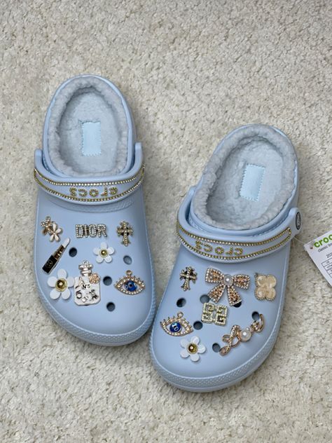 Cream coloured carpet with light blue crocs with gold charms and chains White Crocs Jibbitz Aesthetic, White Crocs With Gold Charms, Black Crocs With Gold Jibbitz, Light Blue Crocs With Charms, White Croc Jibbitz Ideas, Light Blue Crocs Outfit, Blue Crocs Aesthetic, Blue Crocs With Charms, Croc Jibbitz Ideas Aesthetic