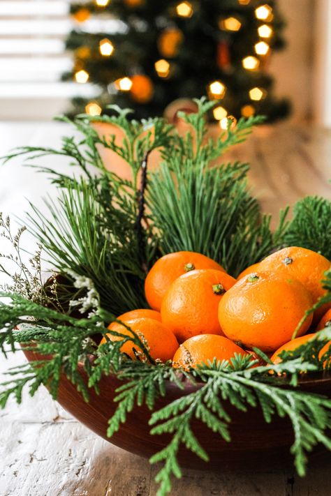 a close up of a wooden bowl filled with evergreens and oranges Decorating With Fruit For Christmas, Christmas Decor With Fruit, Citrus Christmas Centerpiece, Centerpiece With Oranges, Table Decor With Oranges, Christmas Fruit Centerpieces, Oranges With Cloves Decoration, Orange With Cloves Christmas Decorations, White Christmas Floral Arrangements