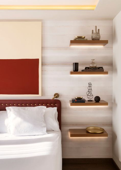 In this modern bedroom, four floating wood shelves with hidden lighting have been installed, with the lowest shelf at the correct height for a bedside table, while the other three shelves have been used to display decorative items. #BedroomDesign #BedsideTable #InteriorDesign #Shelving Floating Shelves As Bedside Tables, Bedside Wall Shelf Ideas, Bedside Shelving Ideas, Bedroom Nightstand Floating, Shelves As Bedside Tables, Wall Shelf Bedside Table, Shelf In Bedroom Wall, Bedroom Floating Shelves Night Stand, Floating Night Stand Ideas Bedrooms