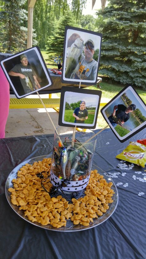 Fishing theme graduation party - table centerpiece I made for my son's high school grad party. Goldfish crackers are scattered around the plate. His fishing lures are in the vase. Printed pictures of him fishing are attached to cardstock and a small dowel rod. -Jill Collins Graduation Party Table Centerpieces, School Centerpieces, High School Grad Party, Fish Centerpiece, Fishing Theme Party, Graduation Party Table, Graduation Table Decorations, Graduation Dinner, Senior Graduation Party