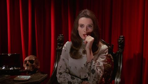 The character Diane, played by Celeste Yarnall, in the 1971 erotic horror movie The Velvet Vampire. She is sitting on an ornate wooden chair in front of a velvet curtain. Next to her is a table made from the same dark wood as the chair. On the table sits an open box that looks like a jewelry box, a human skull and a porcelain plate. She is wearing a grey dress with black embroidery. Dress Flowy Sleeves, Vampire Moon, Velvet Vampire, Light Goth, 1970s Movies, Gothic Western, Werewolf Girl, Crystals Rose Quartz, Coquette Black