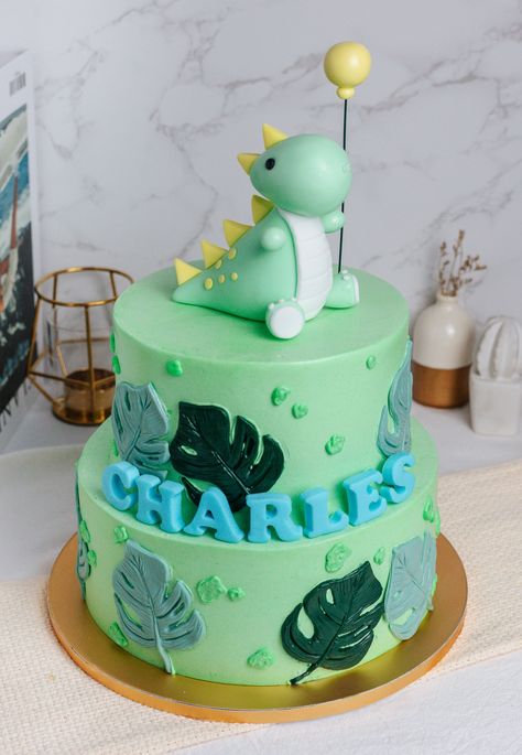 Take a look at this adorable masterpiece, a two-tier pastel green customised cake! Decorated with lush monstera leaves in various shades of green, this cake brings a touch of nature's charm to your celebration. But that's not all! Sitting atop this enchanting creation is an adorable fondant dinosaur, clutching a balloon, ready to bring joy and smiles to your special day. And to make it even more personal, fondant name letters are added, ensuring this cake is uniquely yours. 🦕🎈🎂⁠ Dinosaur Cake For Boys, Simple Dinosaur Cake, Fondant Dinosaur, Dino Birthday Cake, Dinosaur Birthday Cakes, Baby Birthday Themes, Dinosaur Cake, Balloon Cake, Dino Birthday