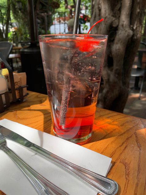 this is about a italian soda on top of a table at a cafe. the soda is clear with a red syrup ombre at the bottom of the clear glass. has a cherry floating on the top and a black straw inside of the  of the drink. two eating utensils, a butter knife and fork at the bottom left under a napkin in the photo on the table surface. Italian Soda Aesthetic, Soda Italiana Aesthetic, Aesthetic Soda, Soda Aesthetic, Local Cafe, Italian Soda, Cafe Aesthetic, Strawberry Syrup, Red Strawberry