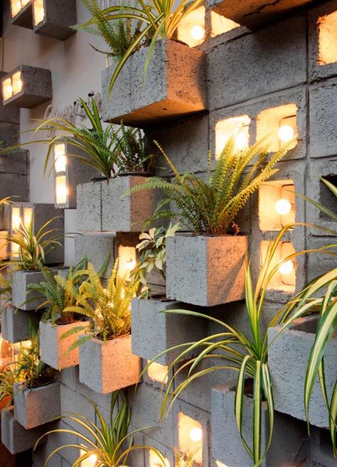 Concrete blocks were used to create this modern eye-catching accent wall, with some of them turned to become planters, slightly protruding to make room for the plants. Other blocks have been turned on their side to make room for individual light bulbs adding a soft glow of the light to the scene. #ConcreteBlockPlantWall #ConcreteBlockPlanter #CinderBlockPlanter Cinderblock Planter, Garden Work Bench, Mediterranean Courtyard, Cinder Block Garden, Garden Wall Designs, Concrete Block Walls, Planter Wall, Landscape Wall Decor, Vertical Gardens