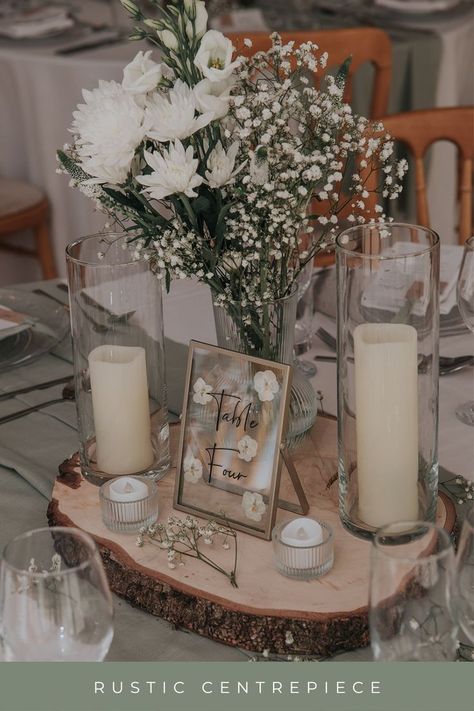 log slice, candles, green and white flowers, table number as a wedding centrepiece Wedding Decor Wood Slices, White Rustic Wedding Theme, Centerpieces Wedding With Table Numbers, Natural Wedding Centre Pieces, Sage Green Wedding Centre Pieces, Wedding Wooden Centerpieces, Centerpieces Wedding Candles And Flowers, Wooden Slice Centerpiece Wedding, Wedding Top Table Flowers Rustic