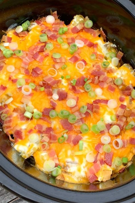 Crock pot of twice baked potato casserole topped with a thick layer of cheese, bacon and green onions