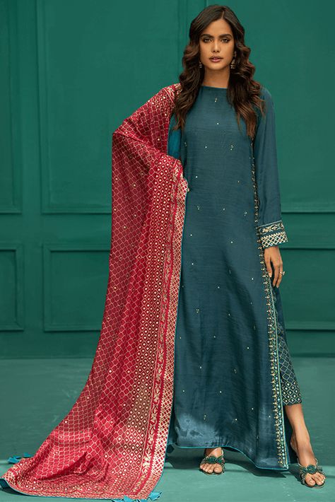 Includes: Shirt Trouser Dupatta Fabric Shirt: PK Raw Silk Pant: Pk Raw Silk Dupatta: Tissue Silk Color: Teal Description: Modern yet elegant, Meraki is a long straight shirt in teal color. The side seam and sleeves are detailed with screen print and hand embroidery. This outfit is paired with matching screen printed and handworked straight pants along with a contrasting deep pink dupatta including print and handwork. This is 3 Piece Stitched outfit. Disclaimer: The color of the outfit may vary d Long Pakistani Suits, Contrast Dresses Pakistani, Eid Special Dresses, Pakistani Eid Dresses, Long Kameez, Pink Dupatta, Pakistani Clothes Online, Festive Attire, Pakistani Dresses Online