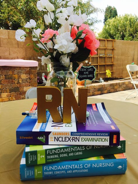 Nursing graduation centerpiece idea! Books and flowers #nursingschool #RN #nursegraduation Nursing Grad Centerpieces, Nursing School Centerpieces, Nursing Centerpieces Graduation, Dnp Graduation Party Ideas, Rose Gold Nursing Graduation Party, Nursing Graduation Party Drinks, Graduation Vision Board, Nurse Party Centerpieces, Registered Nurse Graduation Party