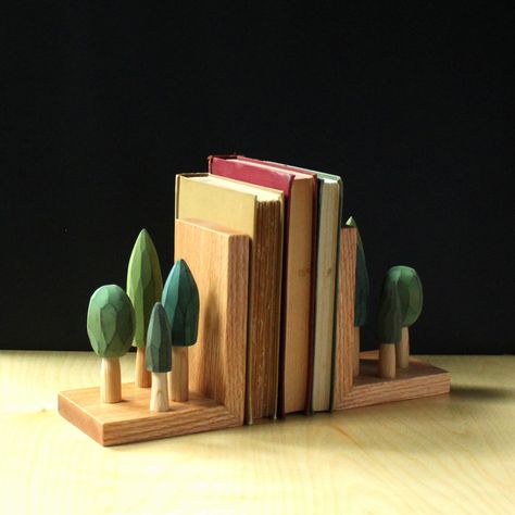 "These hand carved book ends could be the perfect gift for a loved one who is happiest when they are surrounded by trees!  I have carved fragrant cedar wood into these little stands of trees which I then stain in a variety of shades of green before affixing them to the sturdy yet satiny smooth white oak base.  I designed this set to sit on a shelf or mantel and corral books all while looking beautiful.  Each has been built with discreet joinery to last for ages.  A real heirloom quality piece th Wood Projects With Scrap Wood, Book Stand Ideas, Bookends Ideas, Bookends Wood, Wood Carving Projects, Carved Tree, Scrap Wood Crafts, Wood Bookends, Wooden Bookends