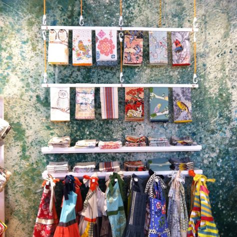 Anthropology in-store wall display of aprons and tea towels. #retail #merchandising #Anthro Tea Towel Display Craft Fairs, Towel Display Ideas, Bamboo Hanger, Tea Towel Display, Retail Wall Displays, Kitchen Booth, Craft Displays, Towel Display, Scarf Display