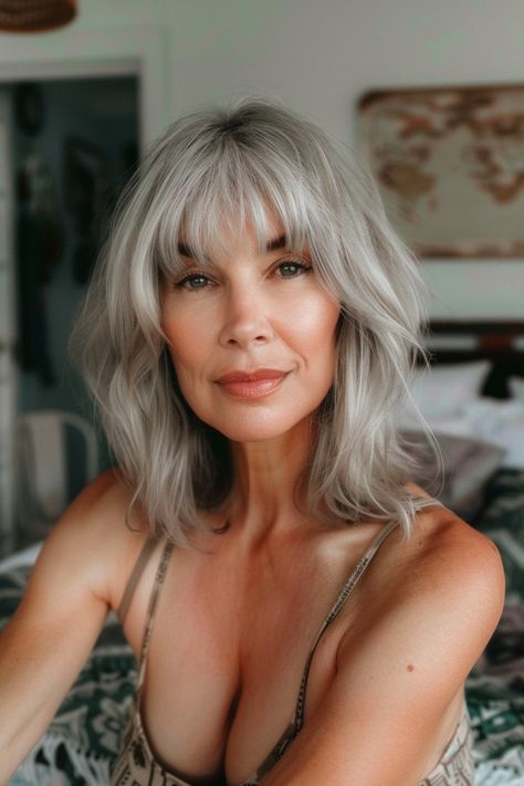 Woman with gray, shoulder-length hair and bangs, sitting indoors and smiling softly. Trendy Gray Hair, Elegant Long Hair, Medium Length Waves, Shoulder Length Wavy Hair, Grey Hair With Bangs, Grey Hairstyles, Silver Haired Beauties, Grey Hair Transformation, Medium Length Layers