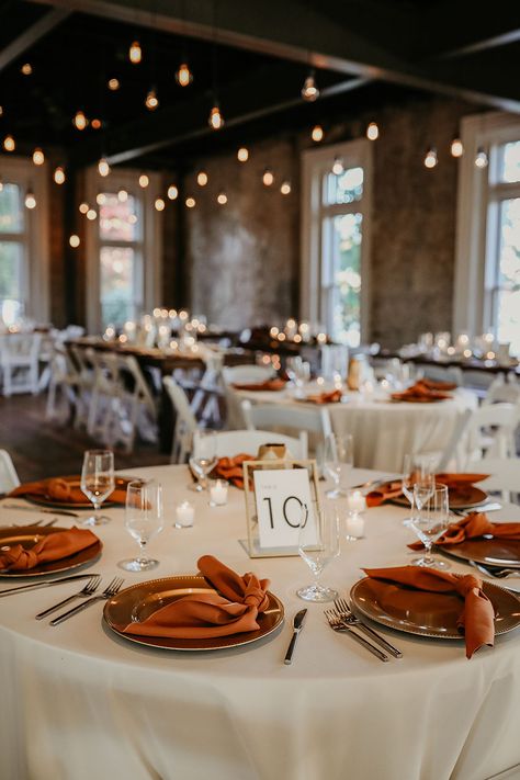 Fall Wedding Reception Table Decor with Rust Silk Napkins and White Linens | Edison Bulb Lighting Fall Wedding Table Linen Ideas, Round Table Wedding Decor Burnt Orange, Fall Color Wedding Table Decor, Rust Orange Table Setting, Rust Wedding Ceremony Decor, Subtle Fall Wedding Decor, Fall Wedding Table Linens, Chic Fall Wedding Decor, Fall Wedding Round Tables