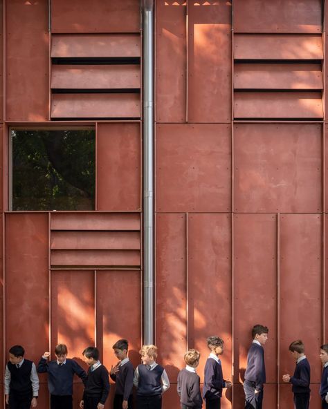 The exterior of the building is clad in Viroc, a composite material that is made using wood fibres and cement particles. Vertical panelling and protruding fins made from the material were used to animate its facade. School Theatre, Modular Cabins, Cement Panels, Red Houses, Facade Panel, Victorian Buildings, School Campus, Architectural Photographers, School Building