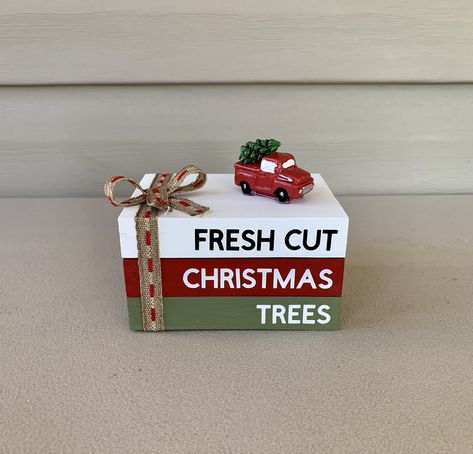 "This handmade mini wooden book stack features 3 rectangle blocks. The blocks are painted white, red, and green with permanent vinyl. The blocks display the words \" FRESH CUT CHRISTMAS TREES \" The blocks are glued together and has a red truck with Christmas tree that is also glued to the top and has a ribbon tied into a bow.  The book stack is about 3\"W x 4\"L x 2.5\" H These will ship in 3 days from ordering Thanks for shopping at  Farmhouse Charm To Love" Farmhouse Christmas Stacked Books, Mini Jenga Block Crafts Tree, Mini Jenga Block Books, Book Stacked In Christmas Tree, 3 Books Stacked Christmas, Stacked Wooden Books Christmas, Mini Jenga Block Christmas Trees, Mini Book Stacks Diy, Christmas Book Stacks