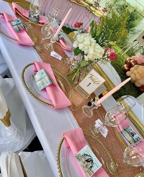 Flaunt an alluring party tablescape by dressing it up with a white tablecloth and spread a blush sequin runner over it for a sparkling appeal. Create an impressive place setting by arranging clear gold beaded chargers with pink napkins and light up pink taper candles for a cohesive look. For a charismatic centerpiece, arrange ivory and pink florals in a clear glass vase. Also, cover your chairs with white chair covers and gold sashes for a stylish display. Pink White Gold Table Setting, Pink Gold And White Party Decoration Table Settings, Pink And Gold Baby Shower Tables, Pink Table Cloth With Gold Runner, Rose Gold Sequin Table Runner, Pink Taper Candles, White Chair Covers, Gold Sash, Pink Napkins