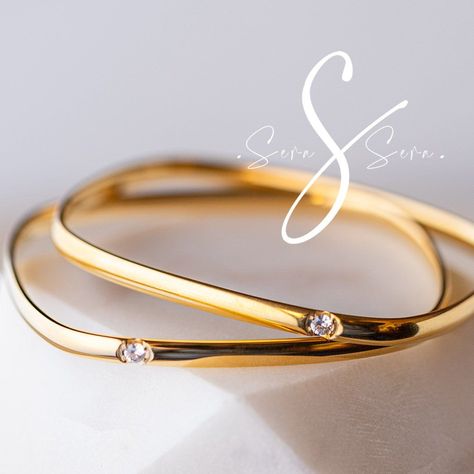 Sounds like an algebra question but it’s not! “ Four Squared” is a bangle crafted from 18k gold plated titanium steel. With a stylishly square design, it is refreshingly minimalist and stacks beautifully with other bangles. Each bangle is set with individual cubic zirconia, making this bling, sing! Although we call this four squared, it's actually a rectangle.... but, Unlike my algebra, this beautiful piece is an A++ This is a slip over your wrist bangle that unfortunately won't fit everyone and.#jewelrylover #handcraftedjewelry #jewelryinspiration #jewelrydesign #jewelryobsessed #jewelryoftheday #jewelrygoals #jewelryfashion #jewelrytrends Contemporary Bangle Design, Minimalist Bangles Gold Bracelets, Modern Bangle Designs, Women Bangles Gold, Solid Gold Bangle Modern, Gold Bangle Set Designs, Plain Gold Bangles For Daily Use Modern, Gold Kada Design For Women Unique, Square Gold Bangles