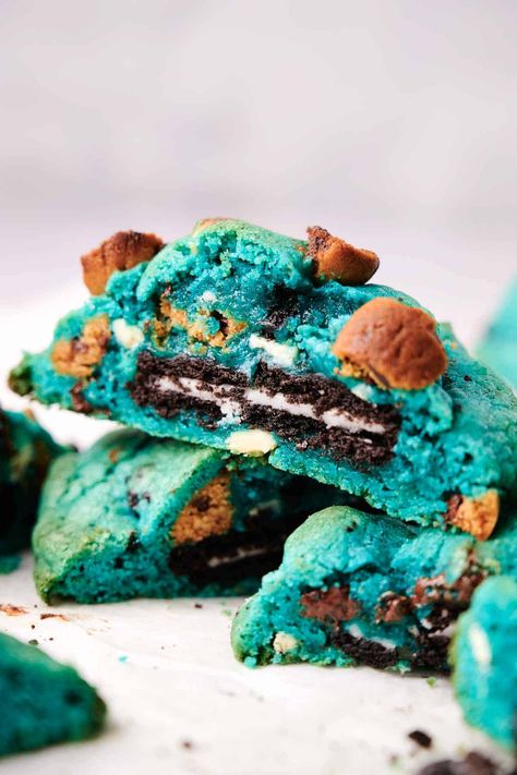 A close-up of a stack of vibrant blue Cookie Monster cookies, some broken to reveal a chocolate and cream center, located on a white surface. Small brown chunks are visible within the blue cookie dough. Cookie Monster Blue Cookies, Cookie Monster Cookies, Mexican Cocktails, Homemade Recipes Dessert, Blue Cookies, Blue Food Coloring, Baking Party, Cheesecake Cookies, Blue Food