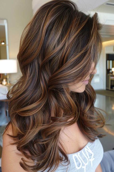 Woman with long, wavy brown hair with highlights styled in loose curls. Carmel Full Highlights On Brown Hair, Medium Brown With Caramel Balayage, Dark Brown Hair With Caramel Highlights Layers, Cool Toned Lowlights For Brunettes, Carmel Highlights On Brunette Hair, Chocolate Brown Hair Caramel Balayage, Caramel Highlights With Curtain Bangs, Colored Highlights In Dark Brown Hair, Layered Dark Hair With Highlights