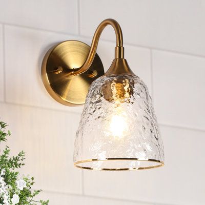 Update your sophisticated bathroom, living room, or bedroom with this glam 1-light wall sconce. This wall sconce brings a sleek silhouette and ambient light to any room. It's made from iron with a copper-gold finish, and it has a water-grained glass bell shade for an elevated look. This sconce includes a circular backplate and a curved arm that supports the shade. It accommodates one E26, Type A, Max 60W bulb (not included), and it's dimmer-switch compatible to set the mood. With its minimalist Brushed Bronze Bathroom Fixtures, Bath Tub Lighting, Gold Bathroom Light Fixtures Wall Sconces, Boho Family Room, Art Deco Wall Sconces Vintage, Antiqued Brass Sconces, Vintage Gold Wall Sconces, Powder Room Lighting, Gold And Glass Wall Sconces