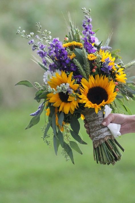 a bold wedding bouquet made of sunflowers, purple and white blooms and much greenery and wheat Wheat And Eucalyptus Bouquet, Sunflower And Lilac Bouquet, Sunflowers And Lilacs, Purple Black Sunflower Wedding, Sage Green Bridesmaid Dresses With Sunflower Bouquet, Wedding Dress Sunflower, Sunflowers Bouquet Wedding, Sunflower Pampas Bouquet, Western Wedding Sunflowers