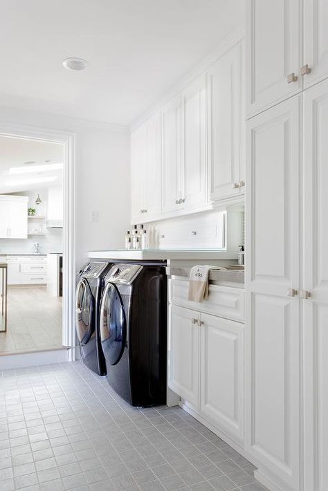 White galley laundry room finished with gray grid floor tiles, black front load washer and dryer, and white stacked cabinets. Laundry Room Subway Tile, Cozy Laundry Room, Gray Laundry Room, Transitional Laundry Room, Wood Tile Bathroom, Grey Laundry Rooms, Laundry Room Tile, White Laundry Rooms, Laundry Room Art