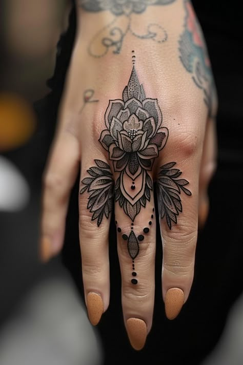 Hand with an intricate black and gray flower tattoo covering the entire back, extending to the middle finger, adorned with detailed patterns and dots. Thumb Palm Tattoo, Finger Feather Tattoos For Women, Rock Hand Sign Tattoo, Woman Knuckle Tattoos, Lotus Tattoo Finger, Finger Tattoos Taurus, Feminine Ear Tattoos, Finger Mandala Tattoo, Finger Name Tattoos For Women