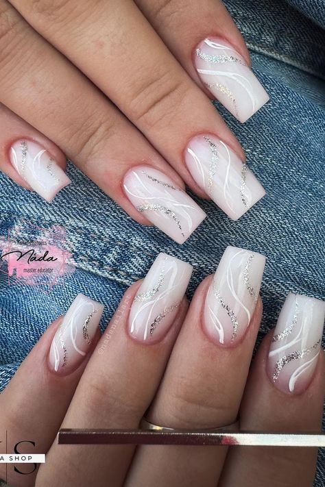 These almond-shaped nails boast an elegant design with a soft pink base that transitions seamlessly into white tips. The nails feature a subtle marble effect created with delicate white lines swirling over the surface. Sparkling silver glitter traces the curving patterns, adding a touch of glamour to this sophisticated look. Perfect for those who love a chic and polished appearance.  // Photo Credit: Instagram @nadanailart White Nails With Silver Lines, Short Square Silver Nails, Nails Airbrush Ombre, Medium Ballerina Nails Designs, Nail Designs With Swirls, White Nails With Lines, White Silver Nail Designs, White Base Nails With Design, Nude Marble Nail Designs