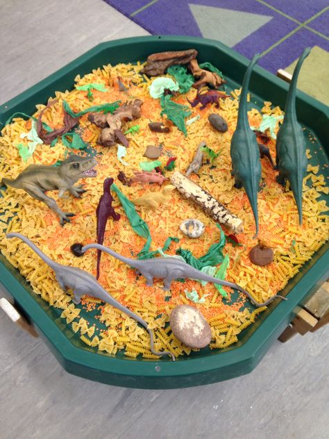 Tough tray dinosaur small world, I used pasta and lentils for texture and added natural resources e.g.  Wood, stones and green and brown shredded tissue paper. Dinosaur Tough Tray Ideas, Dinosaur Tough Tray, Pasta Tuff Tray Ideas, Dinosaur Tuff Tray Ideas, Dinosaur Tuff Tray, Dinosaur Small World, Tuff Tray Ideas Toddlers, Dinosaur Theme Preschool, Dinosaur Activities Preschool