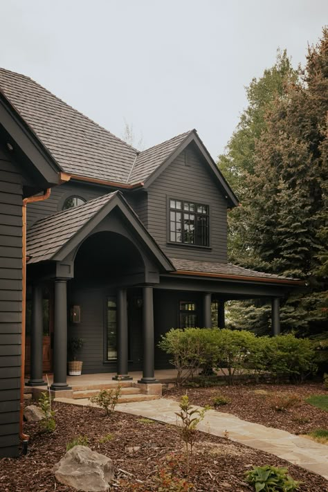 Dark Gray Cottage Exterior, Dark Painted Cottage Exterior, Dark Exterior Paint Colors For House With Stone, Dark House Brown Roof, Charcoal Brown House Exterior, Dark Green Grey Exterior House Colors, Dark House With Light Stone, Dark Green Exterior House Colors Cedar Shakes, Dark Brown Trim Exterior House