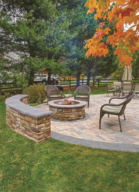 Fall patio scene with boarding seat wall and fire lit fire pit. Three chairs surround the fire pit. Patio table and umbrella can be seen in the background. Hide Concrete Deck Footings, Fire Pit With Wall, Patio With Wall, Half Moon Fire Pit Area, Patio With Retaining Wall, Two Level Patio, Stone Patio Ideas, Fall Patio, Patio Seating Area