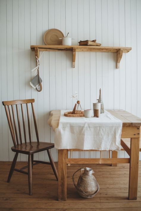 Rustic wooden table and chair against a white paneled wall, with a shelf above holding decor items. Scandi Cottage Interior, Organic Farmhouse Style, Scandinavian Farmhouse Interior, Scandinavian Cottage Interior, Scandinavian Farmhouse Kitchen, Danish Cottage, Scandi Cottage, Modern Scandinavian Farmhouse, Scandi Rustic