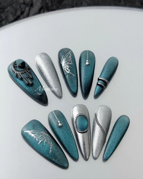 The Celestial Teal Elegance nail set exudes sophistication and mystique, featuring a stunning combination of metallic teal and silver tones. The design showcases intricate details such as a graceful silver butterfly, a dripping crescent moon embellished with a black gemstone, and delicate bead accents. The metallic finish reflects light beautifully, while silver chrome elements add a sleek, futuristic touch. Ideal for those looking to make a bold statement with their nails, this set is perfec... Teal And Silver Nails, Moon Nails Design, Futuristic Elegance, Chrome Elements, Teal And Silver, Silver Nail Art, Teal Nails, Moon Nails, Silver Chrome