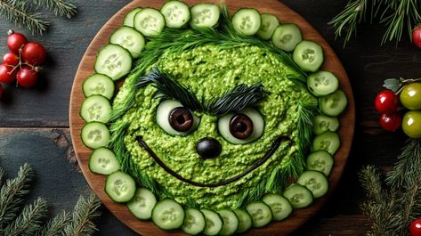 Realistic photo of a Christmas charcuterie board arranged to resemble the Grinch’s face. The face is made with a layer of green foods like guacamole or pesto spread evenly across a circular board. Sliced cucumbers and green grapes outline the face, while black olives create the mischievous eyes and eyebrows. A small red bell pepper slice forms the mouth Christmas Charcuterie Board Grinch, Christmas Guacamole Wreath, Green Christmas Food Ideas, Grinch Dip Recipe, Green Food Board, Grinch Guacamole, Grinch Charcuterie Board, Green Charcuterie Board, Green Appetizers