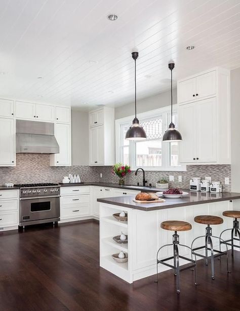 Contemporary kitchen features a beadboard ceiling over a white shaker cabinets adorned with oil rubbed bronze hardware and a gray quartz countertops, Caesarstone Lagos Azul,  and a gray mosaic tile backsplash. A pair of industrial pendants hang over a kitchen peninsula fitted with end shelves lined with backless wood and iron counter stools. Peninsula Kitchen, Kitchen Peninsula, Beadboard Ceiling, Herringbone Backsplash, Condo Ideas, Garage Conversion, White Kitchen Design, Grey Kitchen, Kitchen Redo