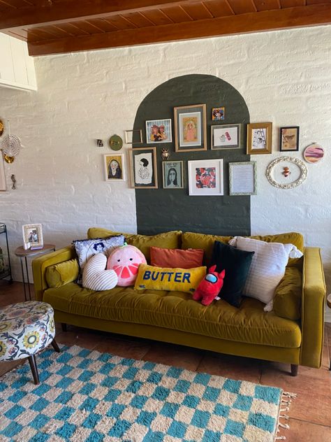 a yellow couch in front of a green arch and blue checkerboard rug. tons of pillows on the couch and a gallery wall on the arch design! Chartreuse Couch Living Room Ideas, Above Couch Wall Decor Eclectic, Yellow Green Sofa, Living Room Art Wall Above Couch, Bright Green Couch Living Room, Behind Couch Wall Art, Arch Behind Couch, Green Couch Eclectic Living Room, Yellow Couch Styling