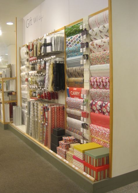 Flat sheets of wrapping paper on the right over dowel rods, a base for stacking gift boxes, acrylic organizers for rolled gift wrap ... plus hooks for tissue paper and gift totes above. Viola! Gift Stores, Gift Wrapping Shop Interior, Gift Wrapping Room Ideas, Paper Store Display, Retail Gift Wrapping Ideas, Wrapping Paper Display Retail, Gift Wrap Display Retail, Wrapping Paper Display, Gift Wrapping Room