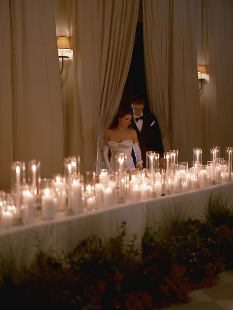 This wedding reception head table was covered in pillar candles and lined with organic florals. The bride and groom were seated with their nearest and dearest bridal party members. The draped ballroom made for the most stunning moody wedding. Candle Reception Table Decor, Moody Wedding Reception Table, Candle Bridal Table, Wedding With Candles Everywhere, Candles And Lights Wedding, Bridal Table Candles, Bride Groom Table Simple, Head Table Candle Decor, Romantic Candle Light Wedding