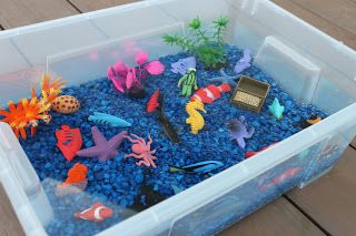 Here's what I put in our bin:  Blue aquarium rocks Plastic aquarium plants (I got all three pictured for $1.00) Safari Coral Reef Toob Pack of plastic fish from the dollar store Coins (for buried treasure)  Then I filled the whole thing up with water!!  I also included a little bucket and a small fishing net so Sweet Girl can "go fishing"! Ocean Sensory, Coral Ocean, Sensory Tubs, Sensory Tub, Sand And Water Table, Sensory Boards, Sensory Boxes, Sensory Table, Sensory Bin