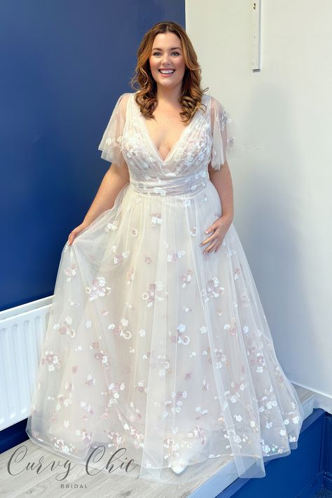 <p>Introducing Gracie, a dreamy plus-size wedding dress that exudes soft romance.</p> <p>Layers of tulle with blush floral sequin detail create an enchanting A-line silhouette. The structured V-neckline and draped bodice gracefully lead to a low back adorned with delicate pearl buttons. Complete with flutter sleeves, Gracie offers various sleeve options and customisations for a uniquely personalised touch. This gown is a perfect blend of whimsy and elegance, ensuring a captivating and unforgettable bridal look.</p> <p> </p> <p>Customisation options available</p> <p class="p1">Sizes: 12, 14, 16,18,20,22,24 and up (no upper limit!)</p> <p class="p1">Have a question about Gracie by Rebecca James Bridal? Just get in touch – <a href="https://www.curvychicbridal.com/contact/"><span cl Plus Size Wedding Dress With Sleeves, Plus Size Bride Dress, Curvy Wedding Dress Sleeves, Curvy Bride Wedding Dress, Wedding Dresses Curvy Bride, Size 20 Wedding Dress, Wedding Dresses For Plus Size, Wedding Dresses With Short Sleeves, Plus Size Wedding Dresses Curvy Bride