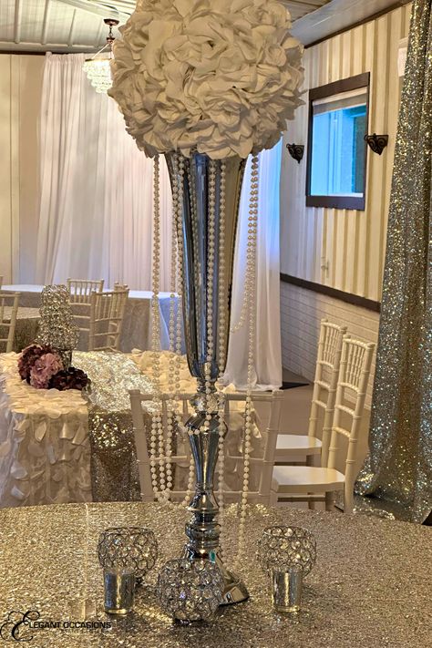 Silver sequin table cloth with stemless crystal beaded goblet votives and a table number surrounding a white flower ball on top of a tall silver trumpet vase draped with pearls Diamonds And Pearls Birthday Party Theme, Pearls And Diamonds Party Theme, Diamond And Pearls Party Theme, Pearl Anniversary Party, Diamonds And Pearls Theme Birthday, Diamonds And Pearls Theme, Pearl Wedding Centerpieces, 60th Wedding Anniversary Decorations, Diamond Wedding Theme