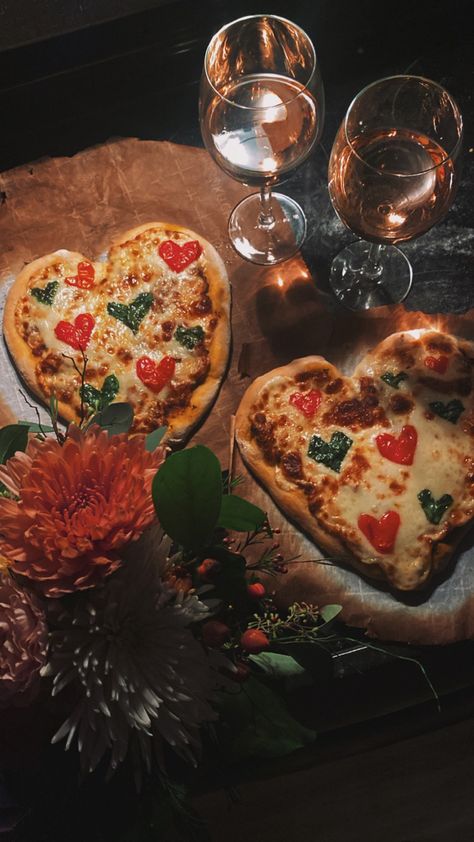 two heart shaped pizzas with heart shaped basil and tomatoes on top. two glasses of wine line the top of the photo and flowers peek in from the bottom. Homemade Pizza Valentines Day, Heart Shaped Pizza Valentines, Heart Shaped Margarita Pizza, Love Dinner Romantic, Heart Pizza Valentines, Love Heart Pizza, Homemade Heart Shaped Pizza, Valentines Aesthetic Pictures, Valentine Vibes Aesthetic