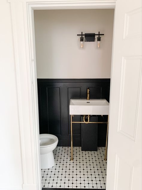 This photo is of a half bathroom with black wainscoting half way up the wall, a gold pedestal sink and black and white penny tile on the floor. Bathroom Black Wainscoting, Gold Pedestal Sink, Black Wainscoting Powder Room, Penny Tile Bathroom Black And White, Black Panelled Bathroom, Black Wanescoting Bathroom, Pedestal Sink Bathroom Ideas Modern, Black Panel Bathroom, Black And White Tile Powder Room