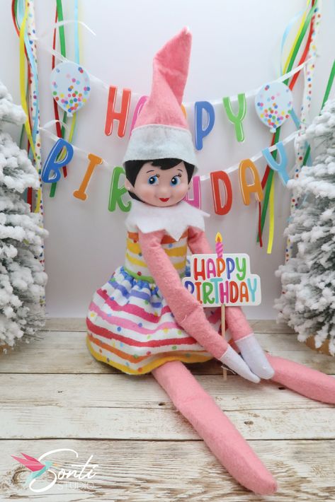 Elf wearing a two-piece rainbow colored dress holding a "Happy Birthday" sign in front of a mini happy birthday banner Happy Birthday From The Elf On The Shelf, Elf On The Shelf For Birthday Kids, Elf On The Shelf Kids Birthday, Elf On The Shelf Happy Birthday, Elf On The Shelf Birthday Party, Elf On Shelf Birthday Ideas, Happy Birthday Elf On The Shelf Ideas, Elf On Shelf Birthday, Elf Birthday Ideas