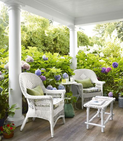 Looks so inviting!  (From Country Living Magazine)white wicker chairs, white columns surrounded by colorful hydragenas Beach House Porch, White Wicker Furniture, Oversized Chair, Wicker Decor, Casa Exterior, House With Porch, Wicker Chairs, White Wicker, Decks And Porches