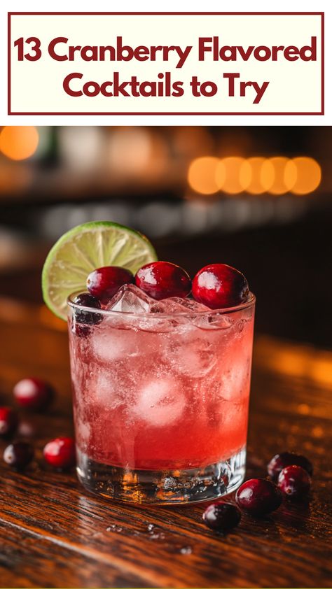 A glass of cranberry-flavored cocktail garnished with fresh cranberries and a lime slice on a wooden table, with vibrant red hues and ice cubes floating inside. Cocktails With Cranberries, Cranberry Mixed Drinks, Cranberry Christmas Drink, Cranberry Vodka Cocktail, Vodka And Cranberry Drinks Cocktails, Cranberry Drinks Alcohol, Cranberry Juice Cocktails, Cranberry Alcoholic Drinks, Cranberry Spritzer Cocktails