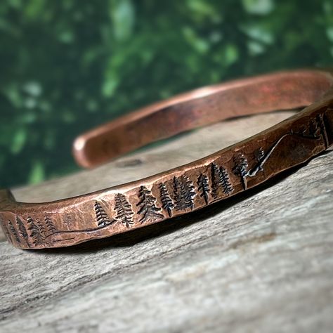 A rustic handmade bracelet that celebrates the beauty of nature and the majesty of the forest with the mountains and trees hand stamped around the rustic copper cuff.   Perfect for the mountain climber or hiker in your life.  This engraved copper bracelet is hand forged and finished with a hammered finish to give it a rustic look, perfect for men and women alike.  Each bracelet is handmade, and no two will be exactly alike. Also please be aware that colors may vary due to viewing screens. If you Mens Copper Bracelet Western, Copper Bangles Handmade, Stamped Cuff Bracelets, Copper Smithing, Hammered Copper Jewelry, Hammered Metal Jewelry, Mountain Bracelet, Mens Copper Bracelet, Handmade Copper Bracelet